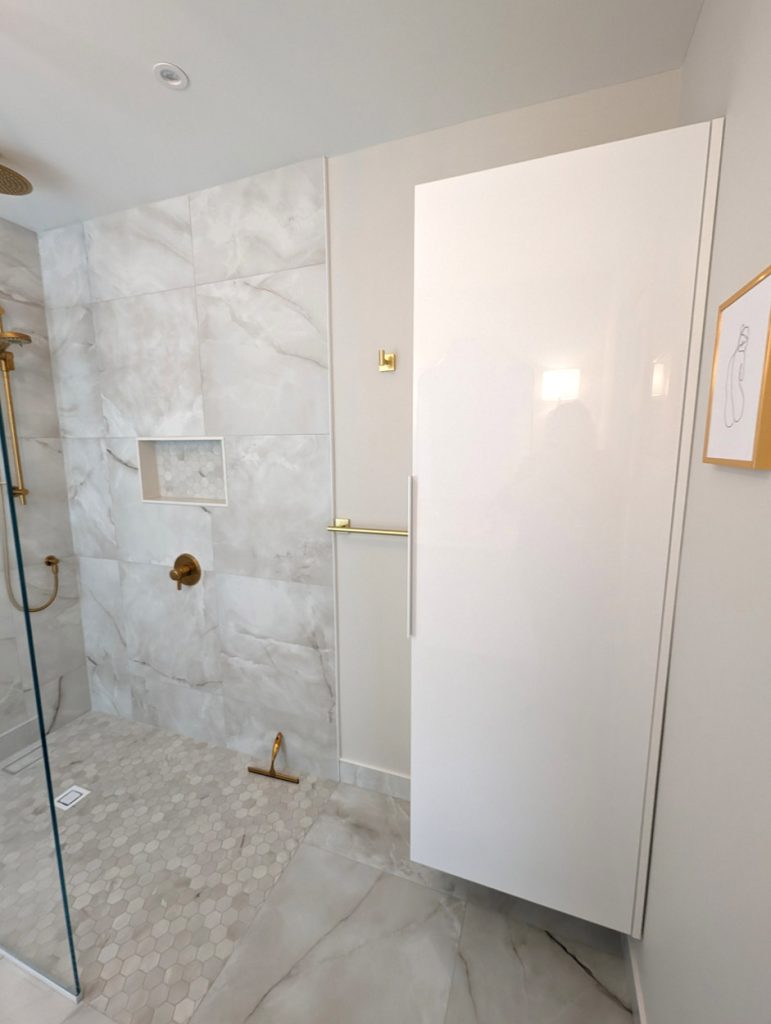 Refined shower entrance showcasing marble-look porcelain tiles, brushed gold fixtures, and minimalist design.