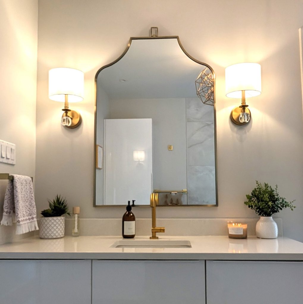 Statement arched mirror framed by modern sconces and gold faucet on a clean white vanity — Lucie Pitt bathroom design.