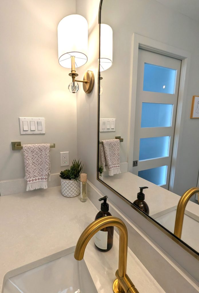 Elegant bathroom details with gold faucet, modern wall sconce, and minimalist styling on quartz countertop.