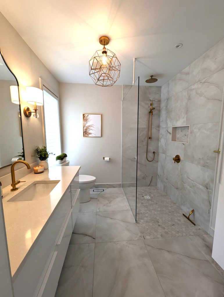 Luxury en suite bathroom with white vanity, quartz countertop, brass fixtures, and marble-look porcelain floors — part of Lucie Pitt’s West Island Luxe project.
