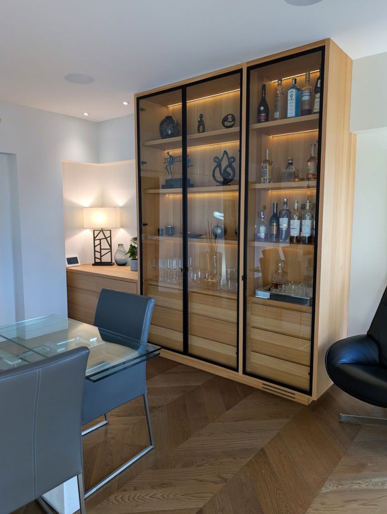 Custom glass display and storage wall with warm wood cabinetry and curated accessories — Habitat 67 interior design by Lucie Pitt.