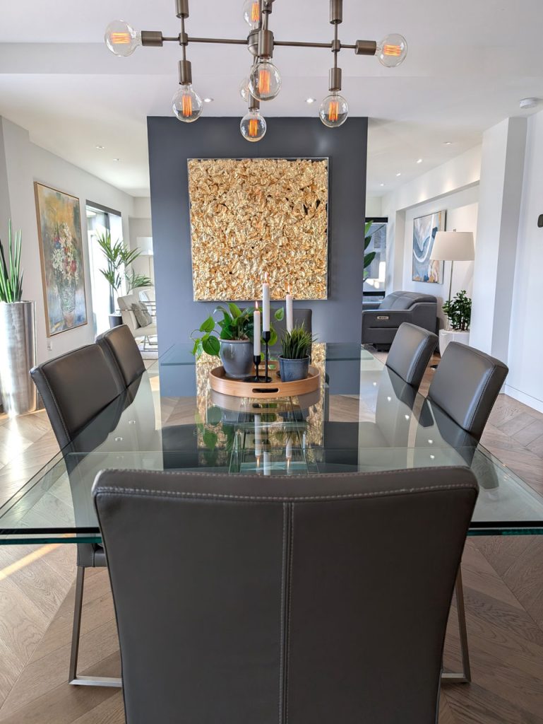 Sophisticated dining room with glass table, modern chandelier, textured art feature, and open-concept layout — part of Lucie Pitt’s Habitat 67 project.