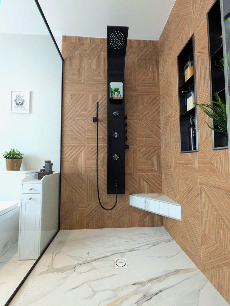 Luxury walk-in shower with black fixtures, warm wood-look tile, and minimalist shelving — part of Lucie Pitt’s Laval Harmony project.