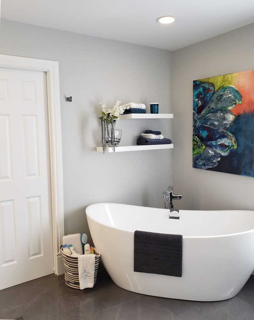 Elegant spa bathroom with freestanding tub, floating shelves, soft grey walls, and modern artwork — from Lucie Pitt’s West Island Spa Retreat project.