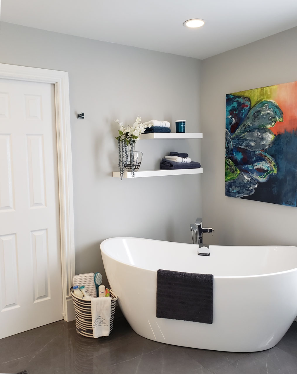 Freestanding bathtub with curated shelving, fresh greenery, and soft grey walls — a tranquil and refined bathroom by Lucie Pitt.